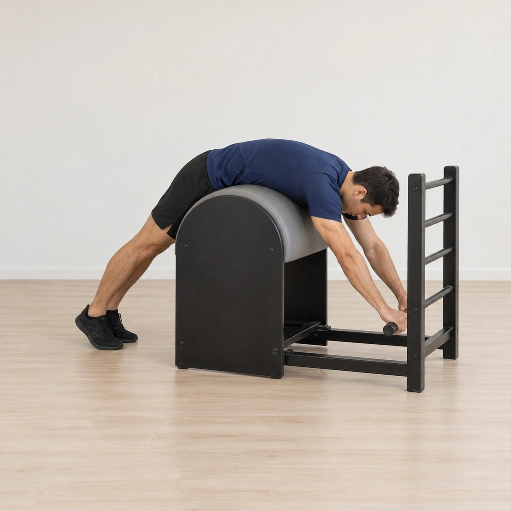 He lies draped over the barrel apex with his hips on it, both hands holding the bottom rung and his legs reaching long toward the floor on the other side.
