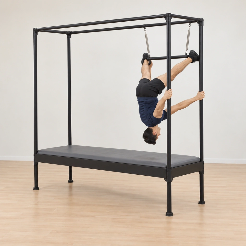 His legs are sent to the top of the trapeze pressed wide against the sprung lines with his ankles pressing in, his inverted body folding at the hips into an upside-down elephant shape held by the rail grip.