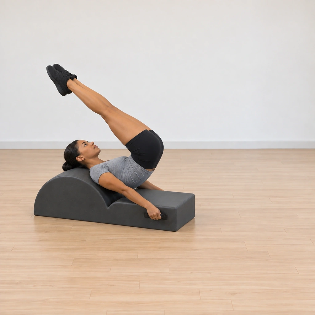 Her legs have lifted and reached over her body toward the barrel above her head, still long and hugging together, her hands holding the handles and her shoulders wide.