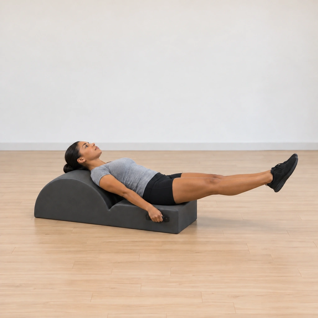 Her legs lower with control toward the mat, still long and hugging together, her head at the barrel and her hands on the handles.