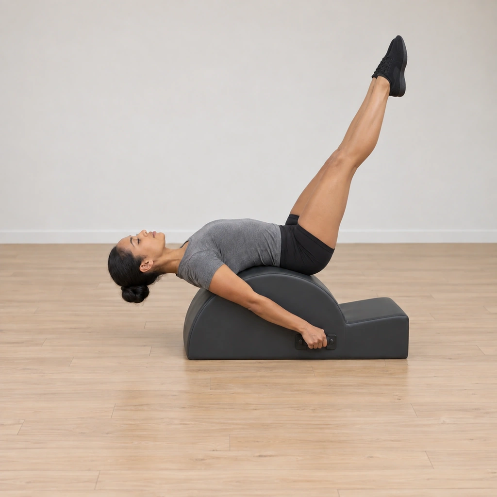 Her legs are straight and lifted nearly vertical above her, toes pointed, while her pelvis and back stay on the arc and her hands hold the handles.