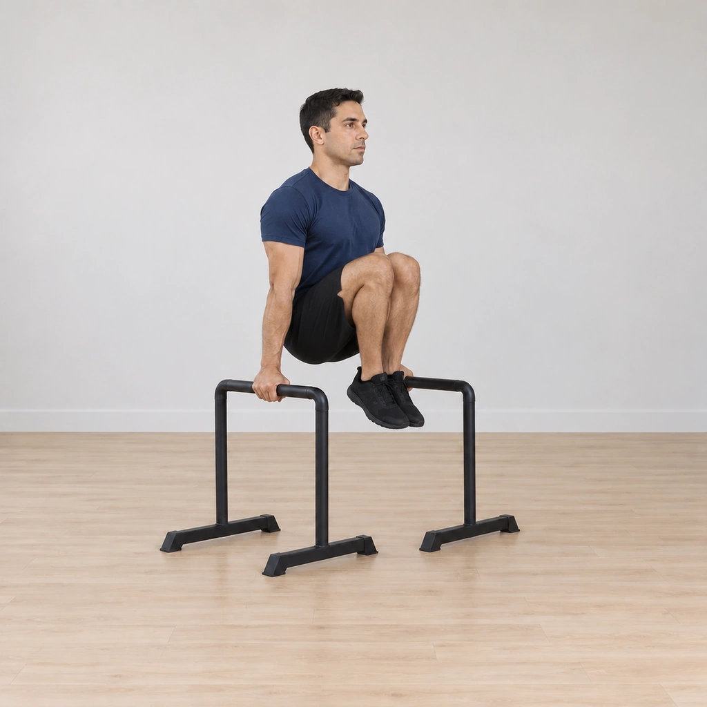 He draws both knees up toward his chest, arms still locked straight, the legs bent and rising under the bars.