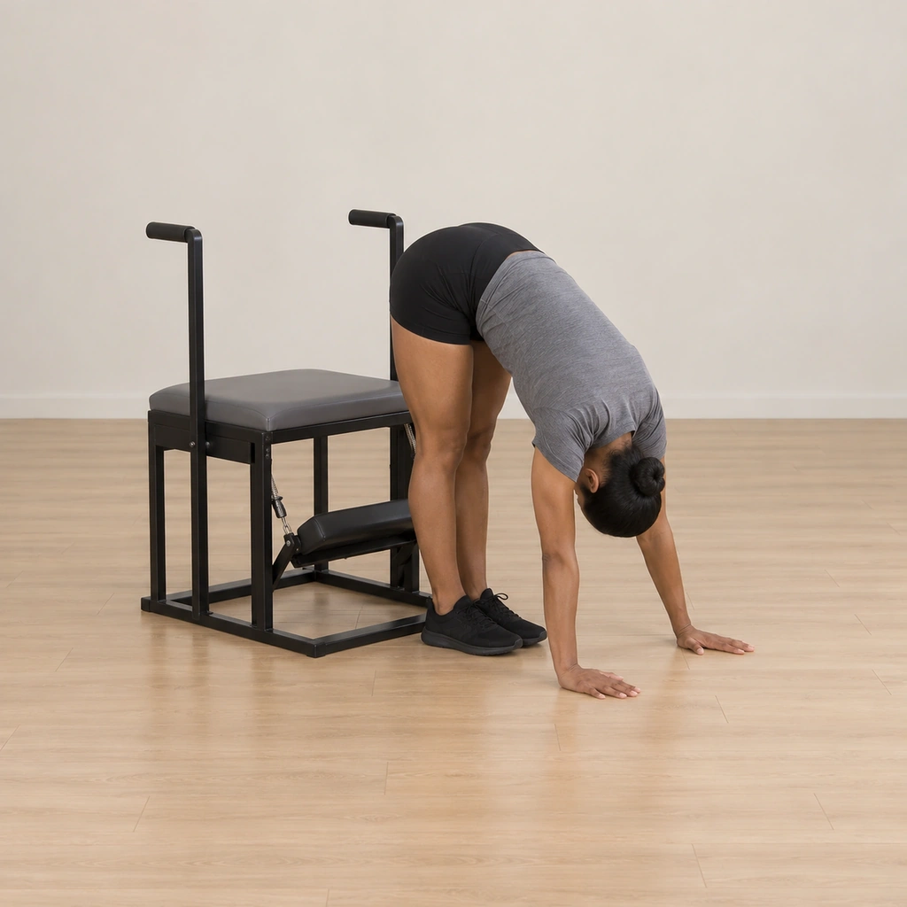 She is folded forward behind the wunda chair with her hands planted on the floor close to it, her head dropped between her arms looking toward the pedal and her back to the chair.