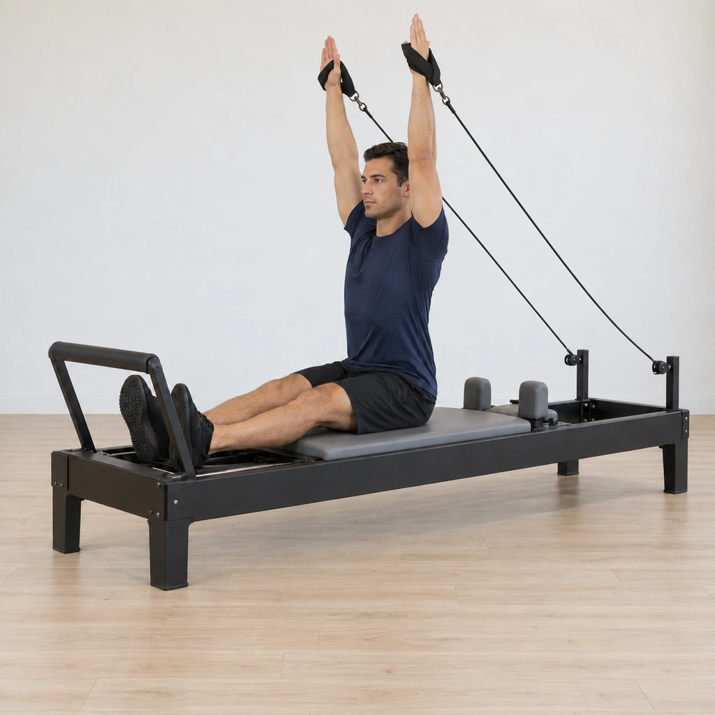 The man exhales lifting both arms overhead with his shoulders rotated so the palms face the footbar, then circles the arms around in line with his body to return toward the tucked start.