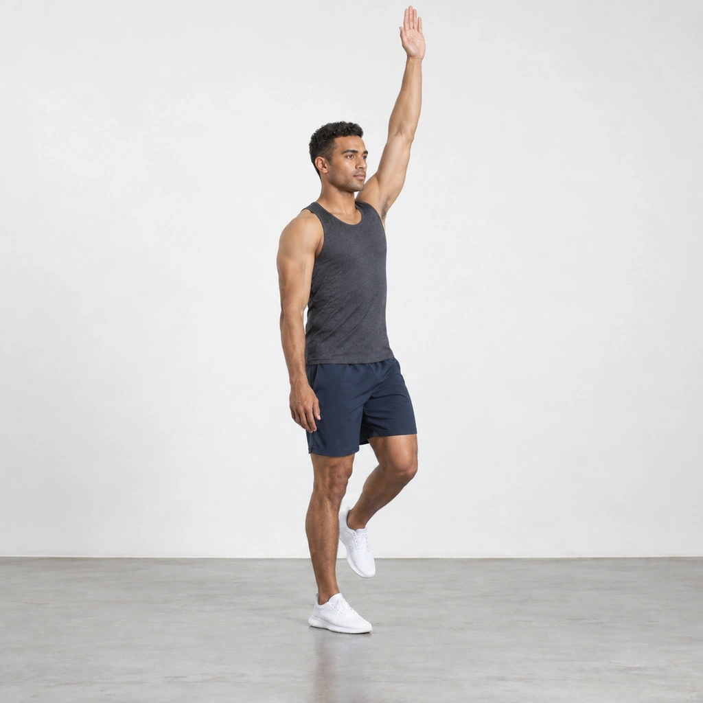 The same man standing tall again on his right leg, left arm now reaching straight up overhead, right arm relaxed at his side, left foot still off the floor.