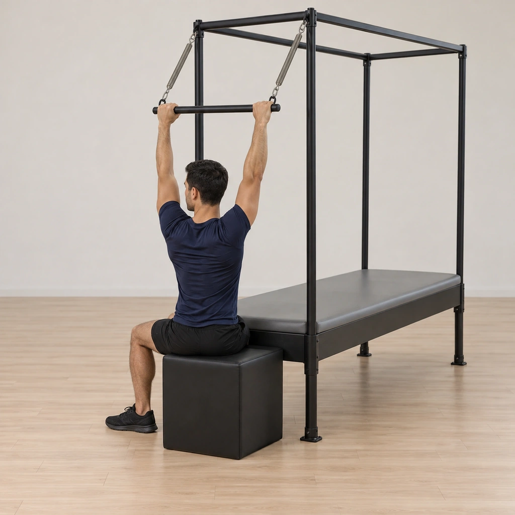 He sits tall on the short box at the table's end, his back to the cadillac, both hands holding the spring-hung push-thru bar with the palms facing out, knees bent and feet pressing the floor.