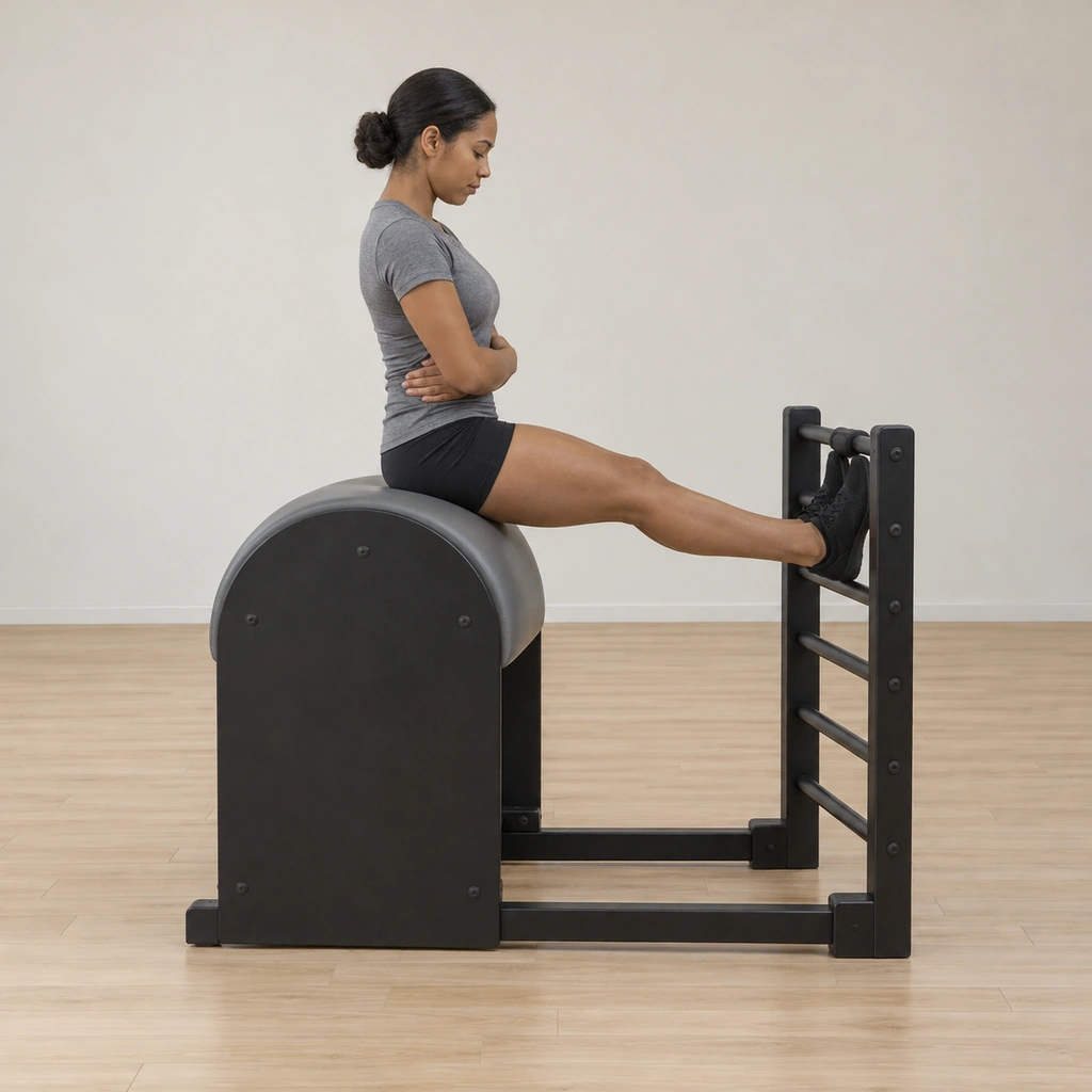 A woman sits on the ladder barrel facing the rungs, her heels on a middle rung and toes hooked under the top rung, sacrum resting on the barrel behind her, arms relaxed.