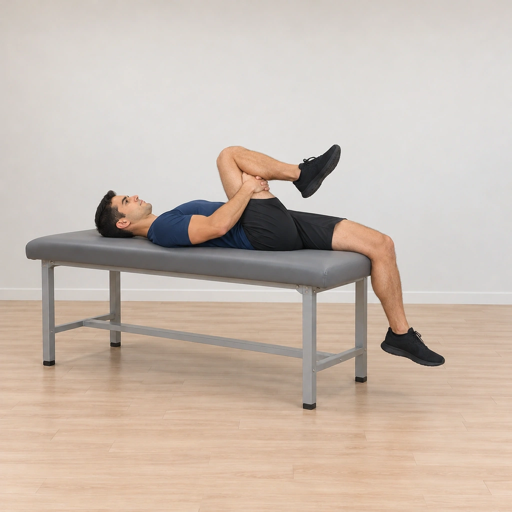 He lies supine on the table hugging his left knee to his chest, his right thigh lowered flat to the table with the bent right knee at the edge and the right lower leg hanging off the table in the stretch hold.