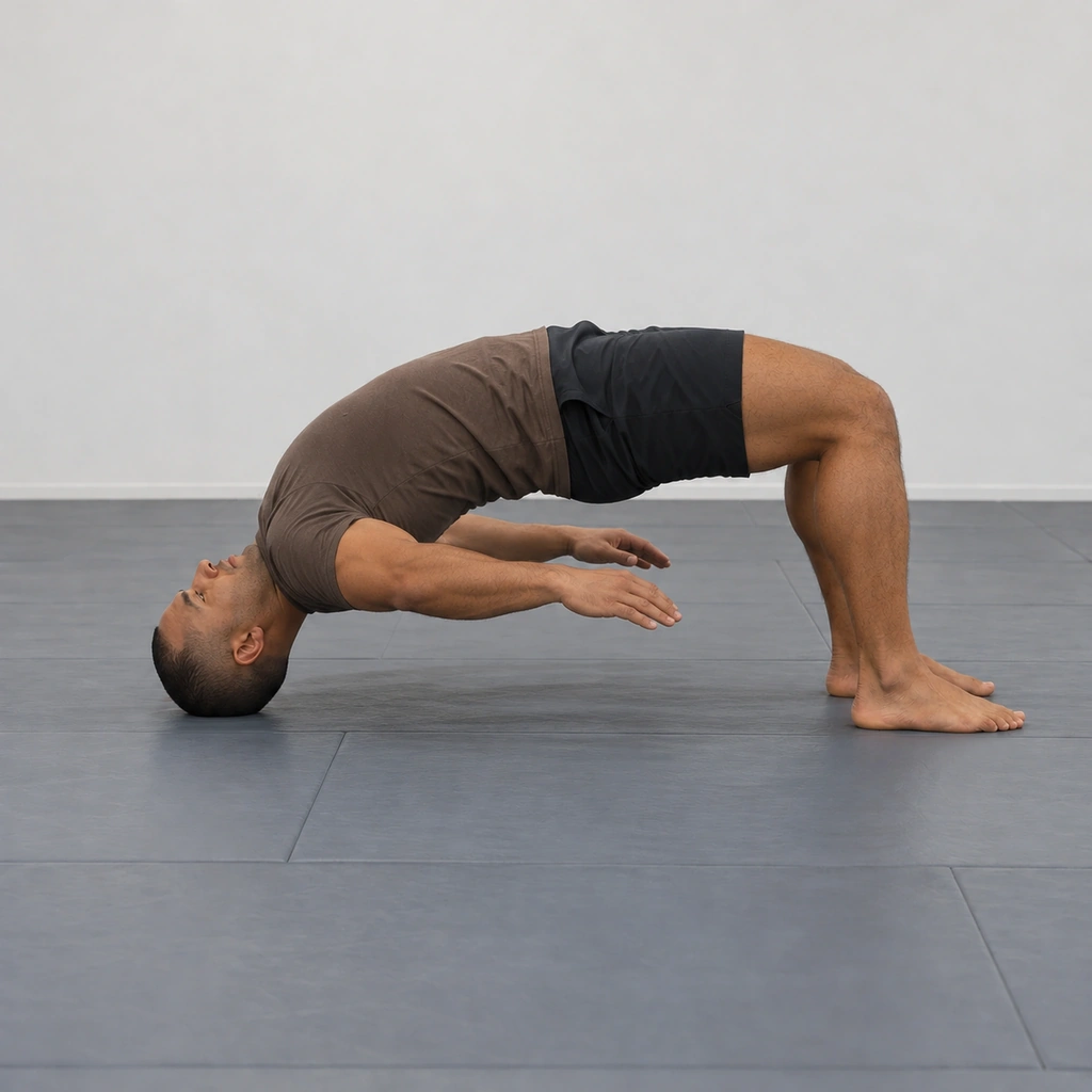 A man in the no-hand neck-bridge hold, the full arch carried on the top of his head and his feet alone, hands lifted from the mat, hips still high.